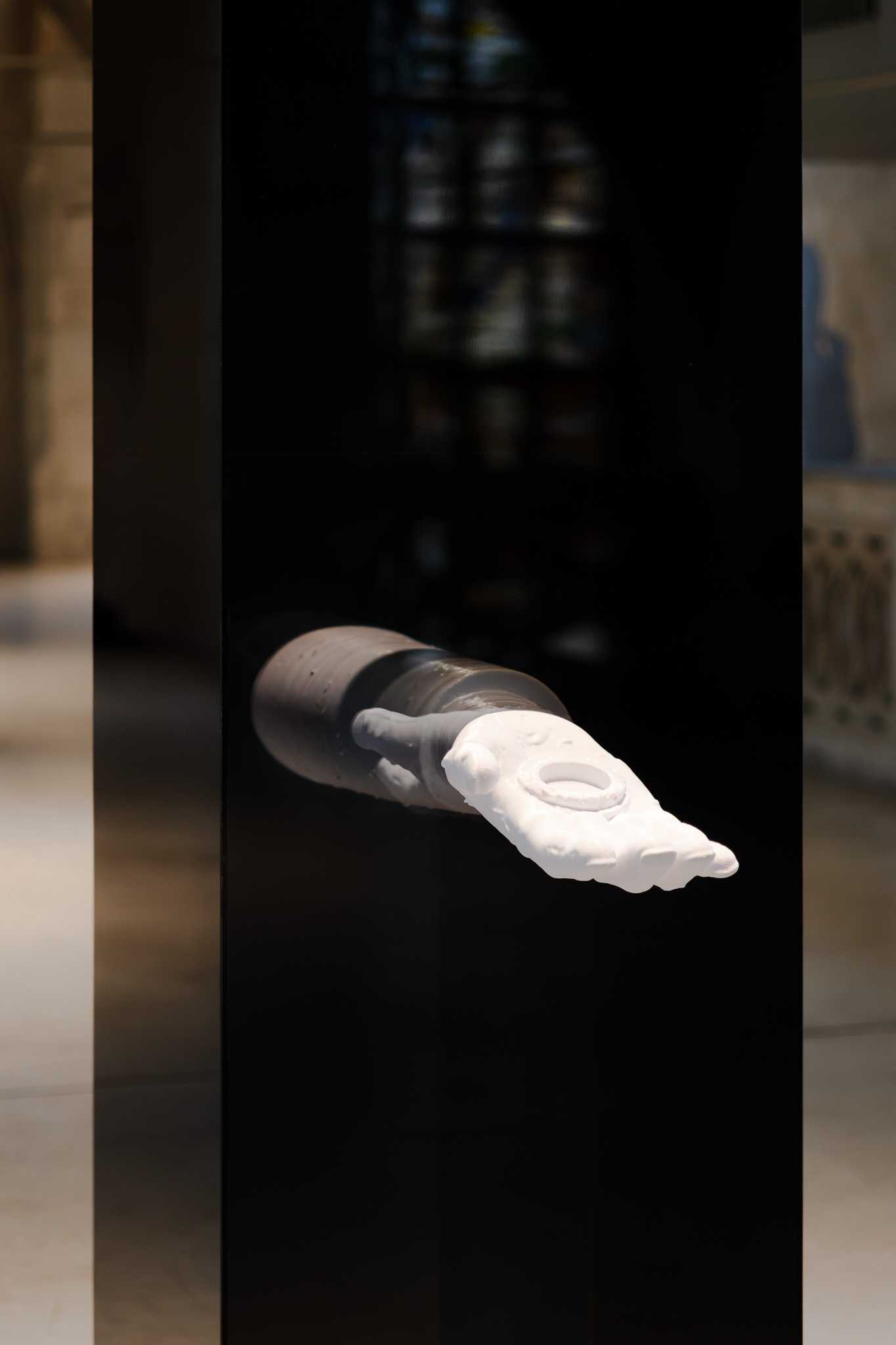 Nahaufnahme des weißen 3D-gedruckten Armreliquiars, das aus der schwarzen spiegelnden Stele tritt.