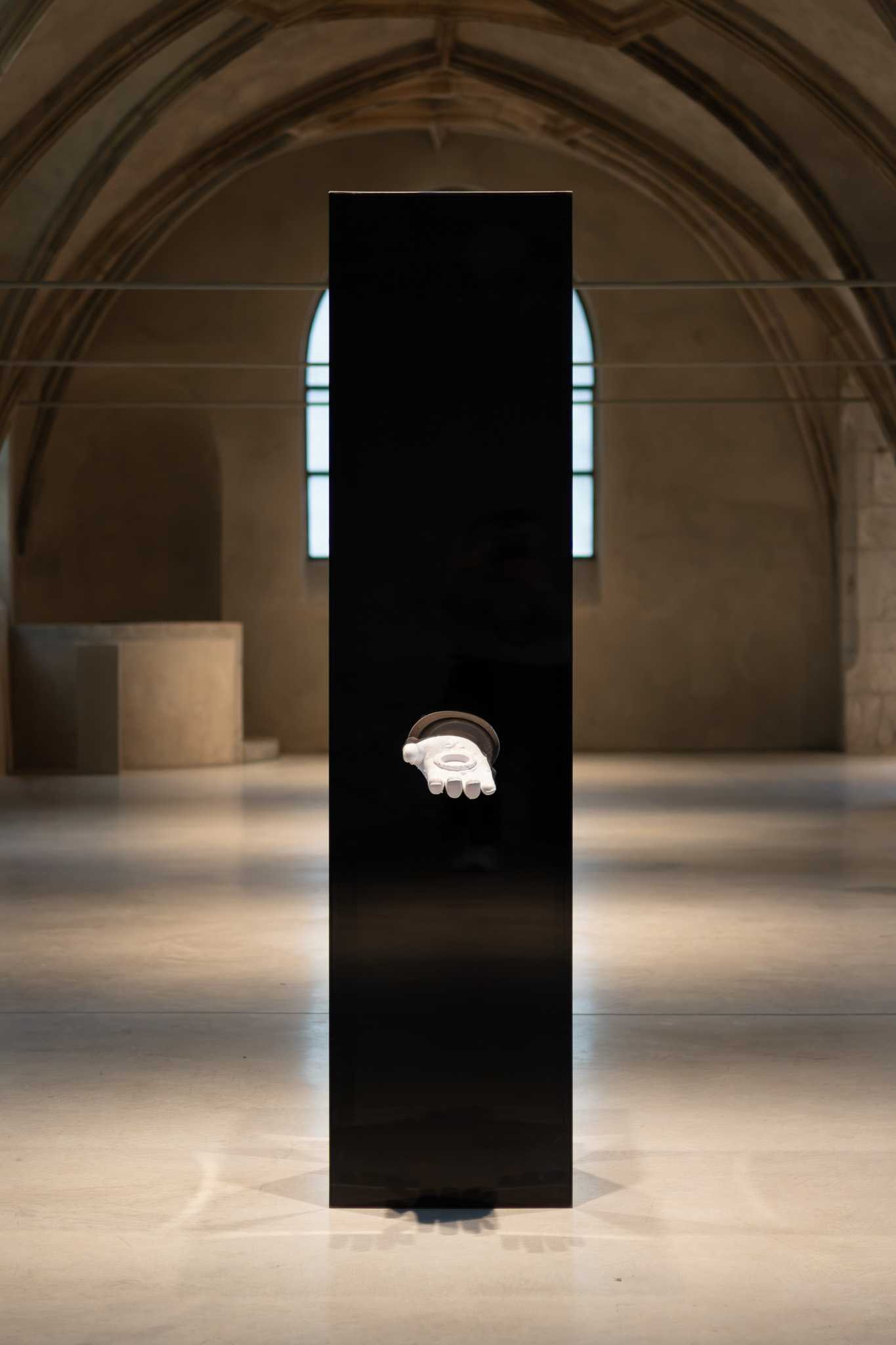 Die schwarze Stele frontal unter dem Gewölbe, dahinter ein Rundbogenfenster, das 3D-gedruckte Armreliquiar ragt aus ihrer Fläche.
