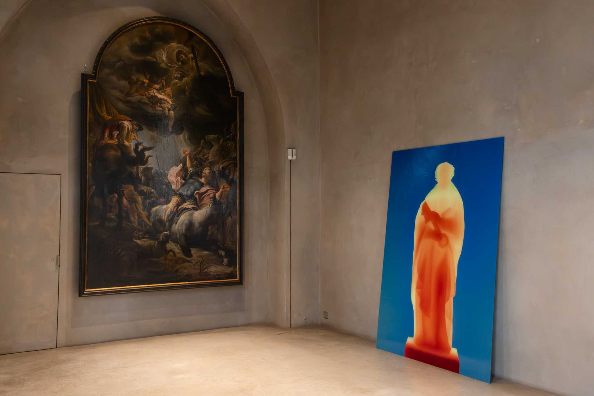 Der Druck lehnt in der Ecke eines Raums, links an der Wand hängt ein großes barockes Altarbild.