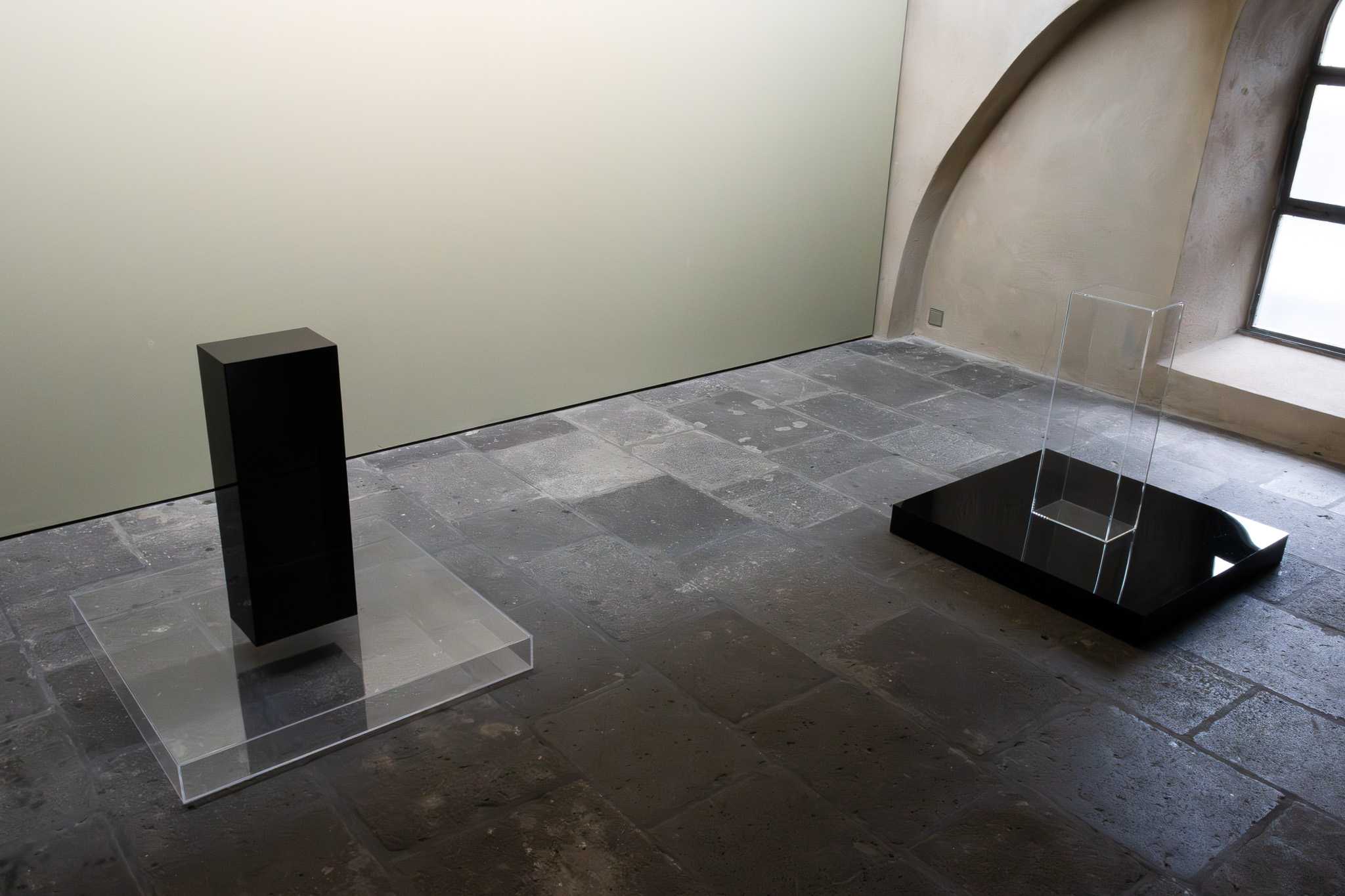 Raumansicht mit beiden Arbeiten: links eine schwarze Säule auf einer klaren Acrylplatte, rechts ein klarer Acrylkasten auf einer schwarzen Platte.