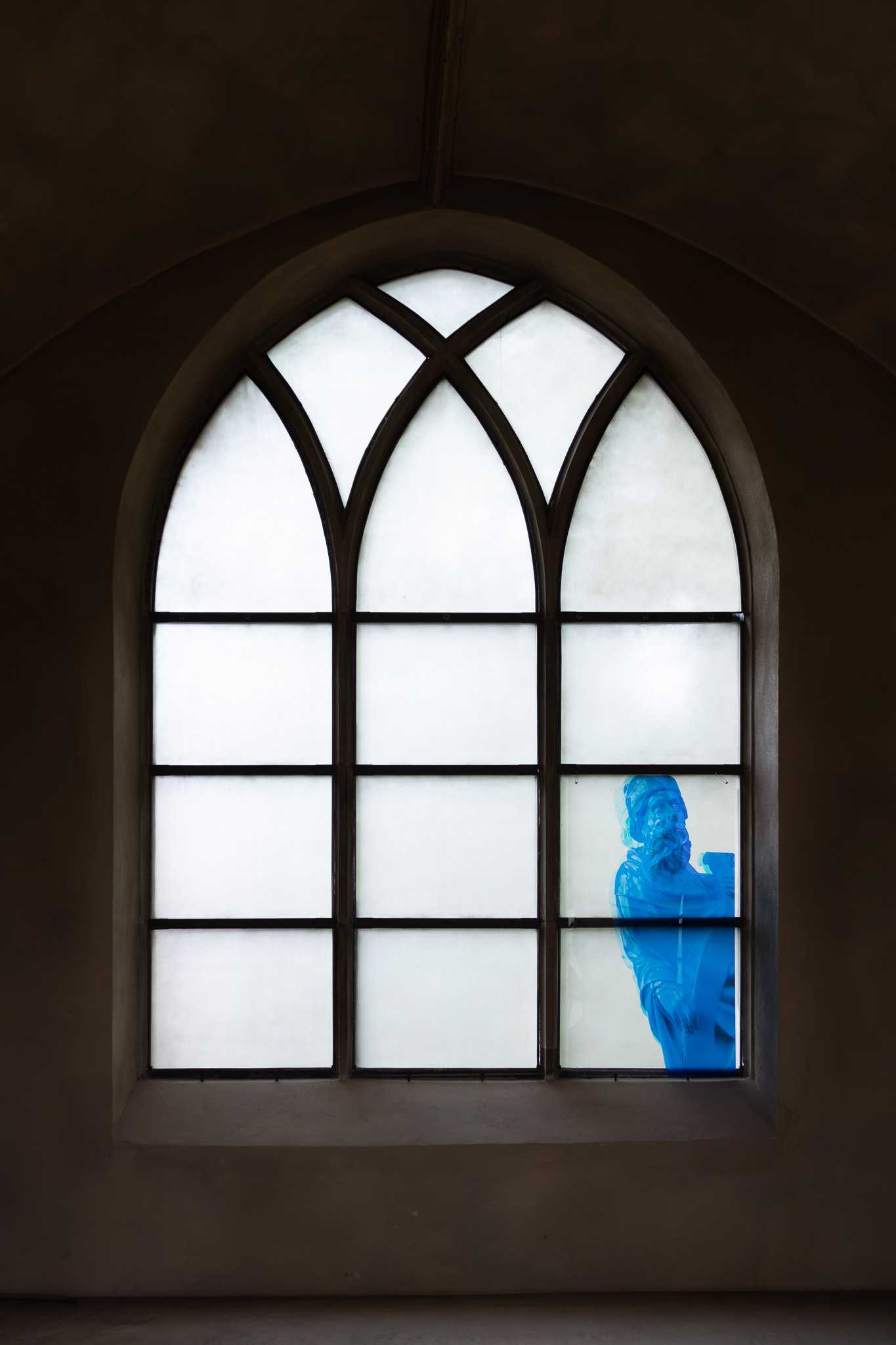 Ein tief sitzendes Spitzbogenfenster mit drei weiß verglasten Bahnen; ein durchscheinender blauer Druck des Propheten mit seiner Schriftrolle füllt die unteren Felder der rechten Bahn.
