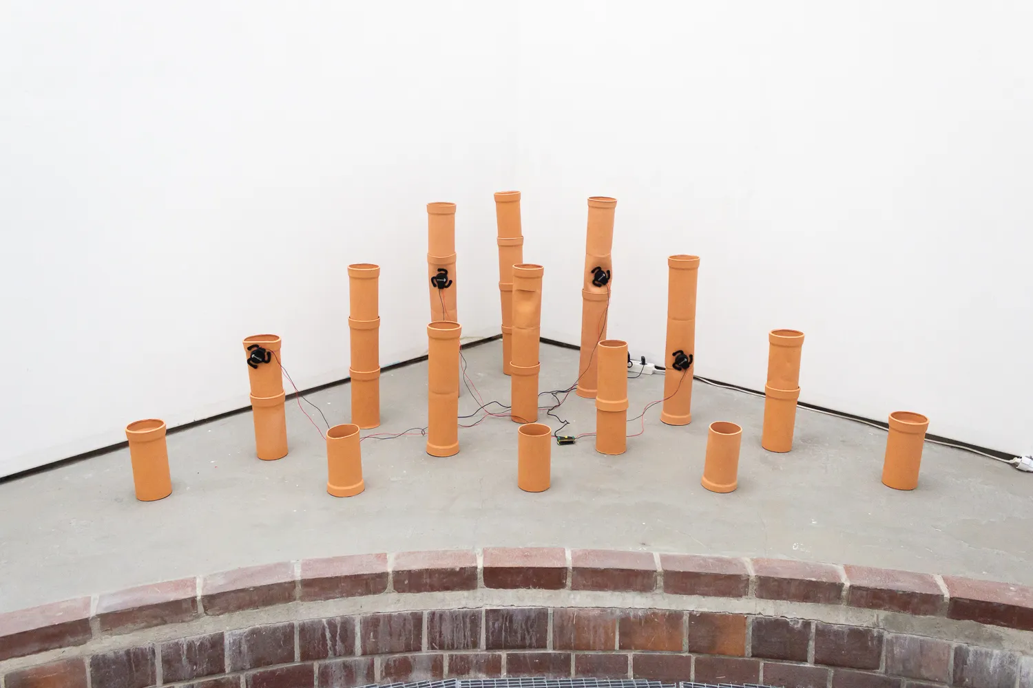 Ceramic pipes arranged in the corner of a room. Four of the pipes have small black electronic devices attached with thin wires running from them.