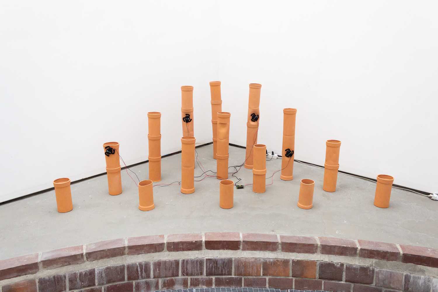 Ceramic pipes arranged in the corner of a room. Four of the pipes have small black electronic devices attached with thin wires running from them.