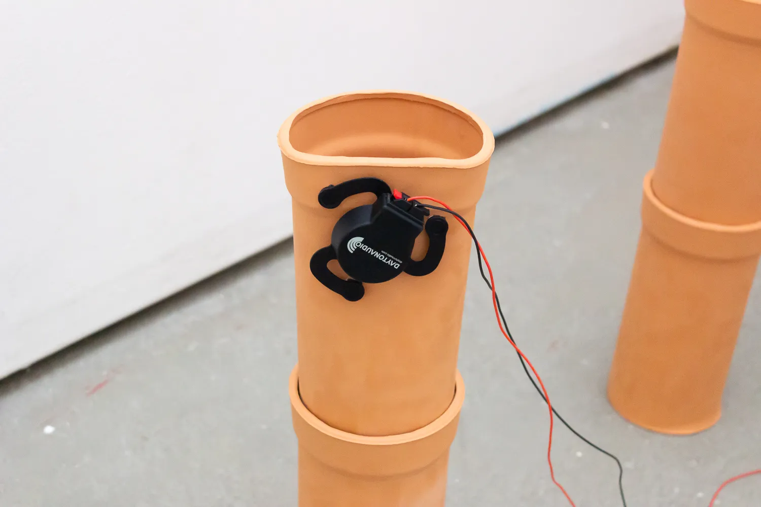 Nahaufnahme eines an einem Keramikrohr befestigten Audio-Exciters mit herausführenden Drähten.