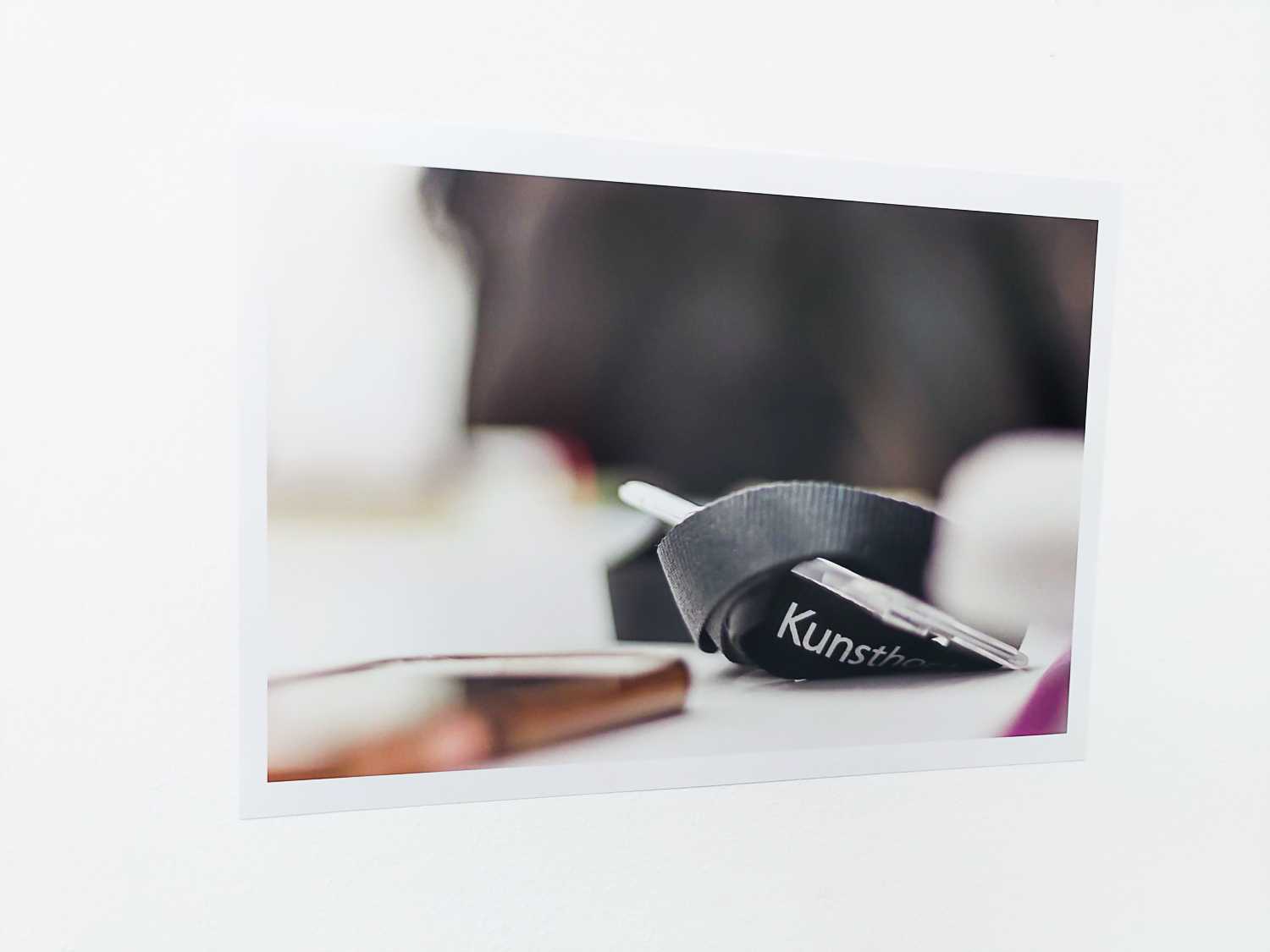 A printed photo of a lanyard with the word 'Kunst' visible, hung on a wall.